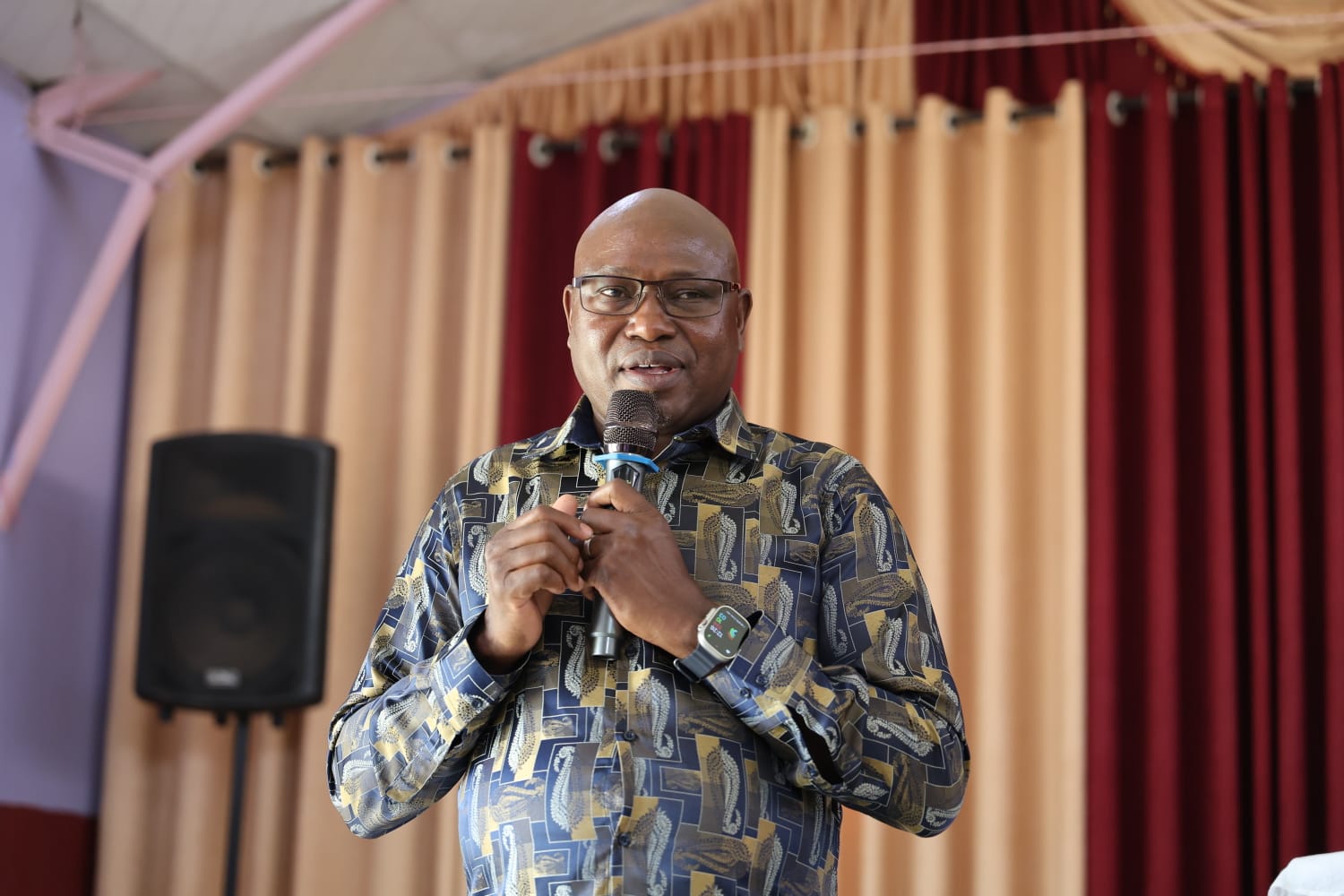Patrick Kiptoo holding a microphone at an indoor gathering.